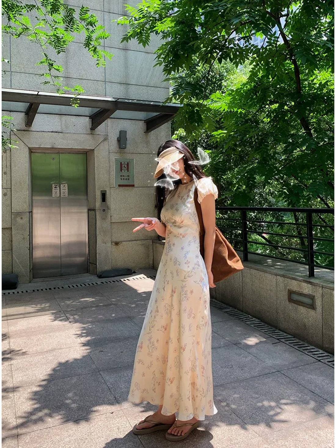 A woman in a cream floral print long dress with puff sleeves and a pearl necklace stands on a paved area.
