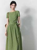 A woman wearing a sage green striped dress with a boat neck and tie belt.