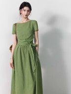 A woman wearing a sage green striped dress with a boat neck and tie belt.