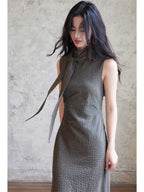 A woman wearing a black gingham floor-length dress with a high neck and tie detail.