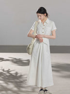 A woman wearing a white A-line dress with a button-front, collar, and twisted waist tie.