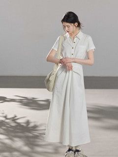 A woman wearing a white A-line dress with a button-front, collar, and twisted waist tie.