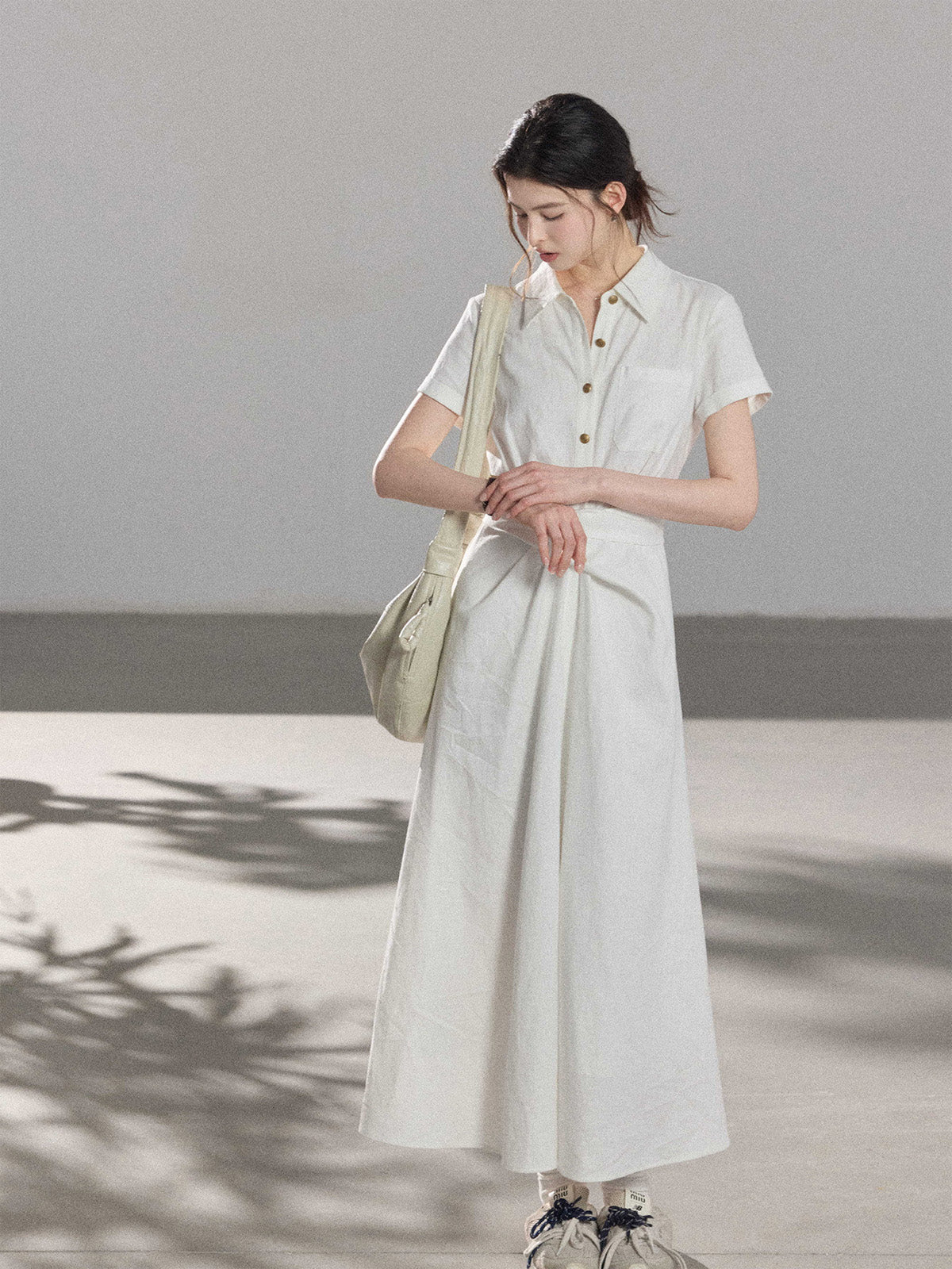 A woman wearing a white A-line dress with a button-front, collar, and twisted waist tie.