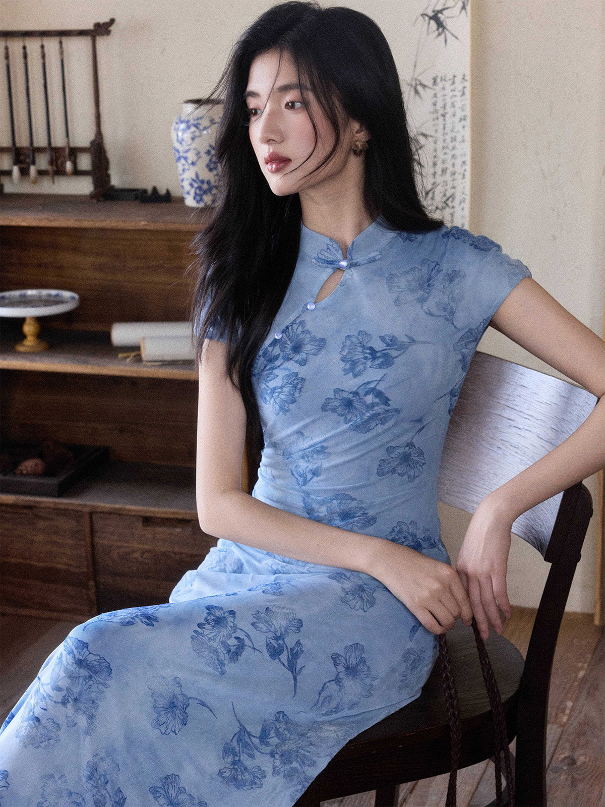 A woman in a light blue floral dress with a mandarin collar and keyhole opening, sitting on a chair.