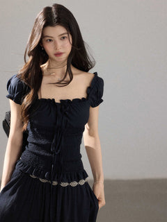 A woman wearing a black long dress with a square neckline, puff sleeves, and a smocked waist.