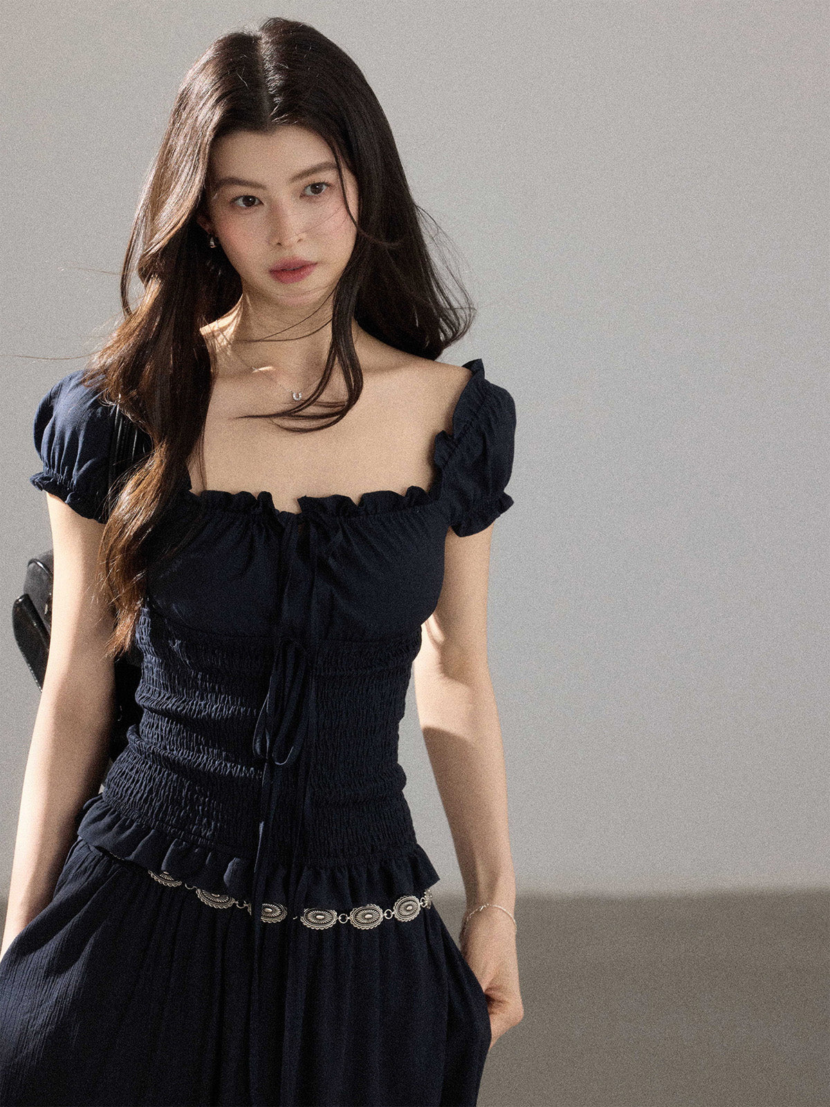 A woman wearing a black long dress with a square neckline, puff sleeves, and a smocked waist.