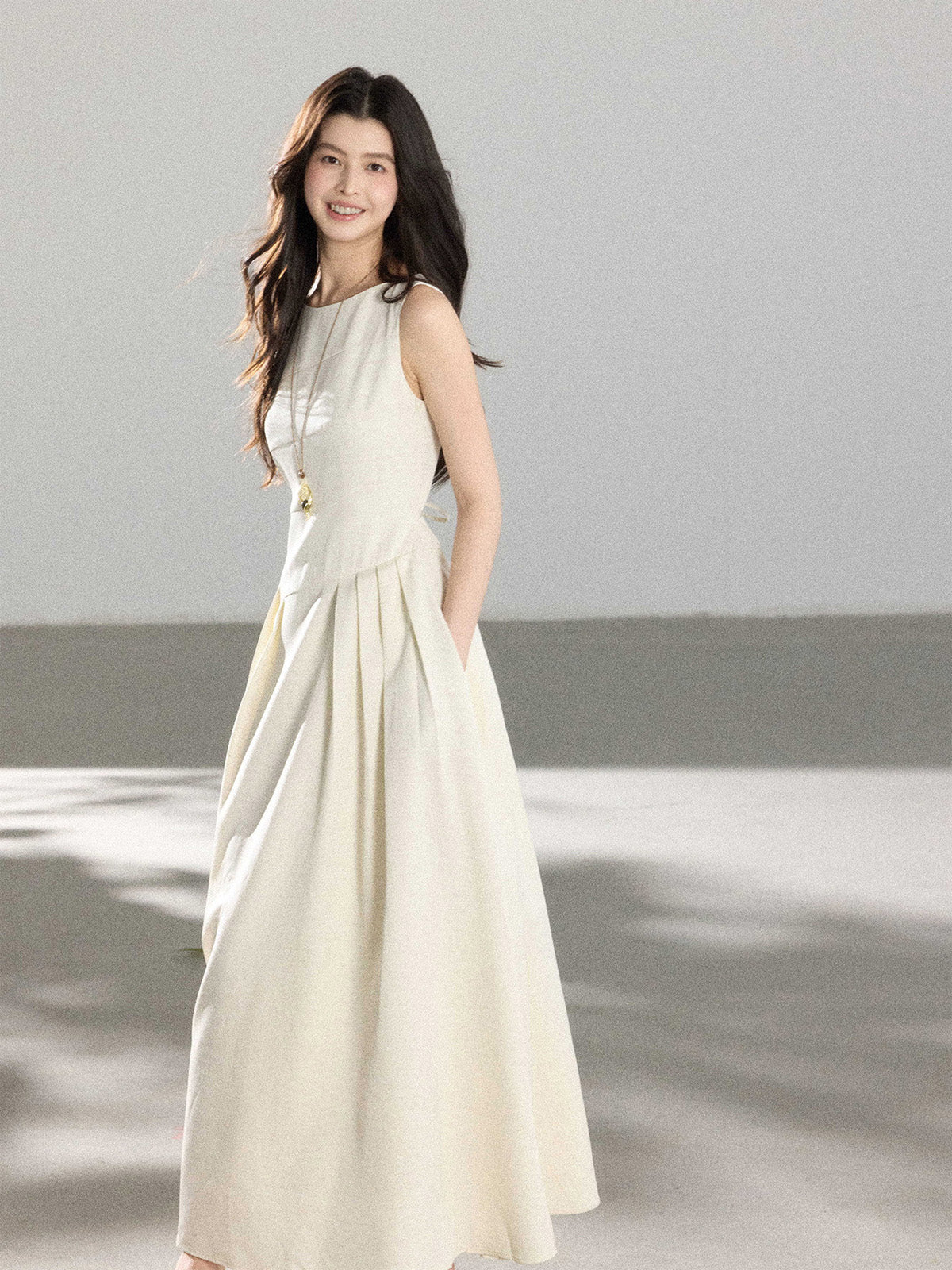A woman in a cream sleeveless A-line floor-length dress with a round neckline and pleated skirt.