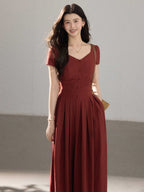 A woman wearing a long red dress with a V-neck, short sleeves, and a pleated skirt.