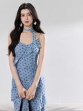 A woman in a light blue polka dot long slip dress with ruffled layers and an adjustable strap.