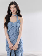 A woman in a light blue polka dot long slip dress with ruffled layers and an adjustable strap.