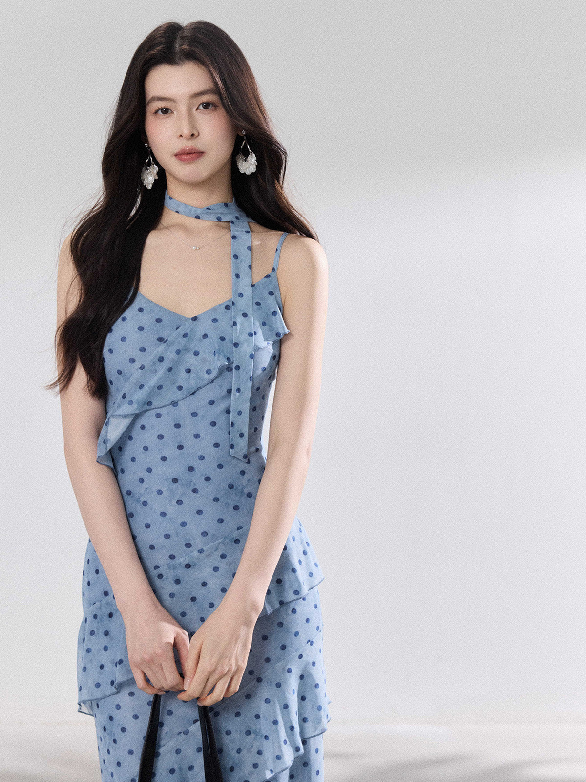 A woman in a light blue polka dot long slip dress with ruffled layers and an adjustable strap.