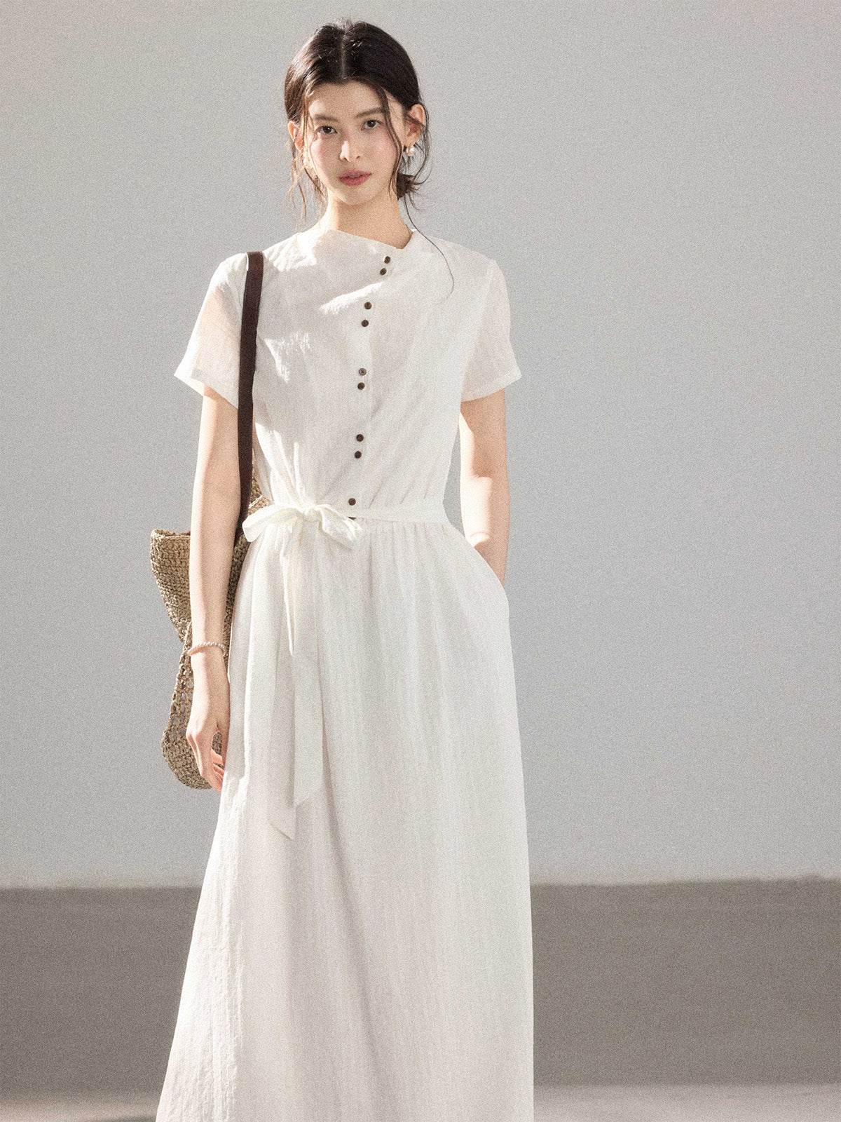 A woman in a white A-line dress with a button placket and tie belt.