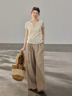 A woman wears a cream-colored knitted top with a V-neck and ribbed trim at the hem, paired with wide-leg pants.