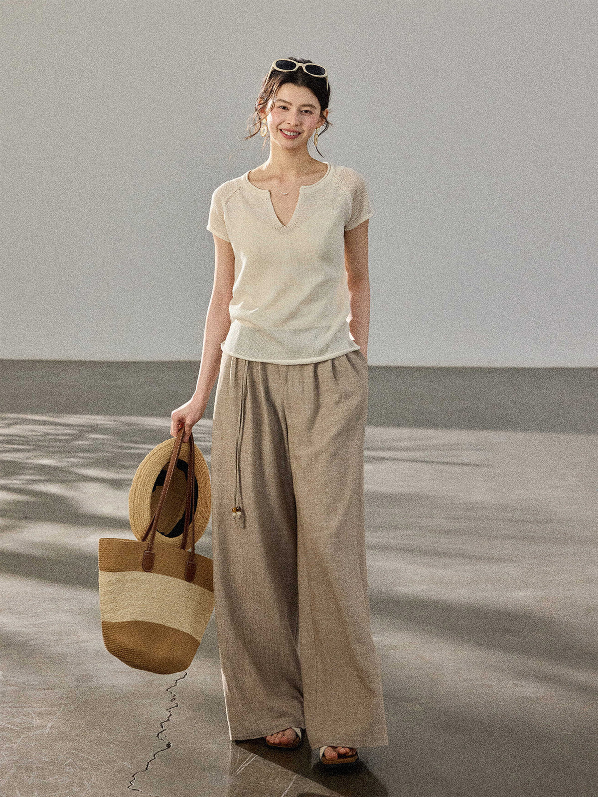 A woman wears a cream-colored knitted top with a V-neck and ribbed trim at the hem, paired with wide-leg pants.