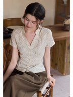 A woman wearing a cream polka dot short-sleeve top with a V-neck and button-front closure.