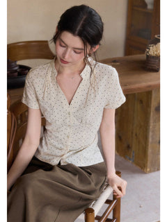 A woman wearing a cream polka dot short-sleeve top with a V-neck and button-front closure.