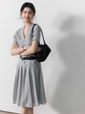 A woman wearing a grey A-line midi dress with short sleeves, a V-neck collar, and a pleated skirt.