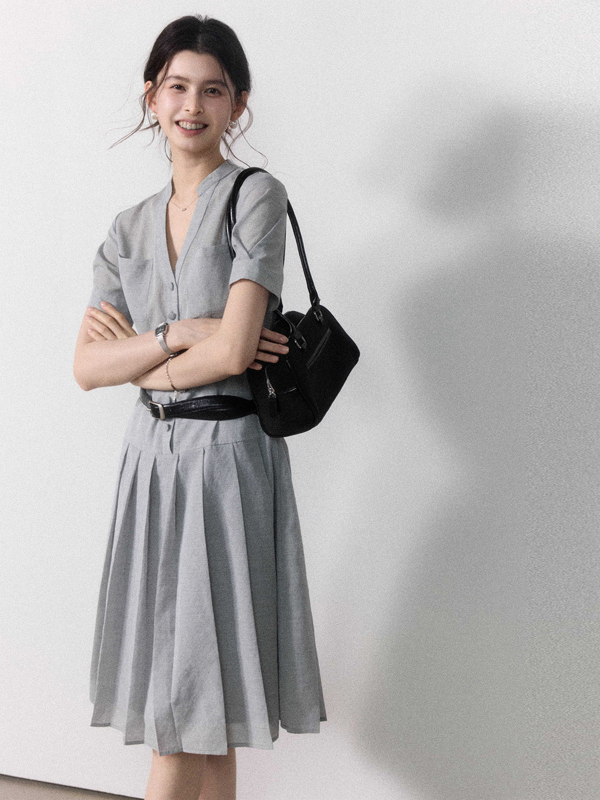 A woman wearing a grey A-line midi dress with short sleeves, a V-neck collar, and a pleated skirt.