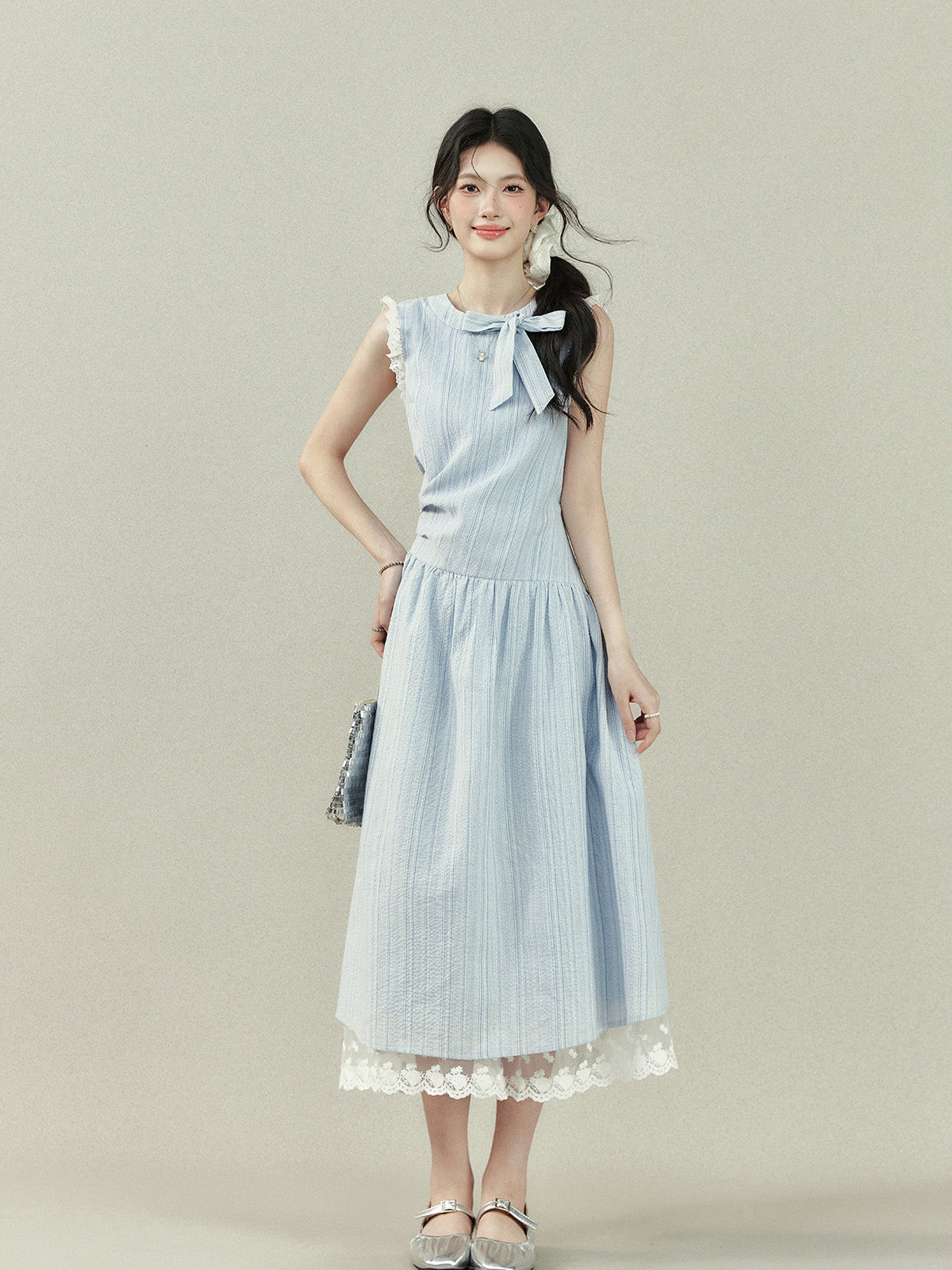 Light blue midi dress with vertical stripes, a bow tie neckline, lace trim on the shoulders and hem, and a gathered waist.