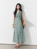 A woman wearing a long, light blue dress with a green leaf pattern and a twisted knot at the waist.
