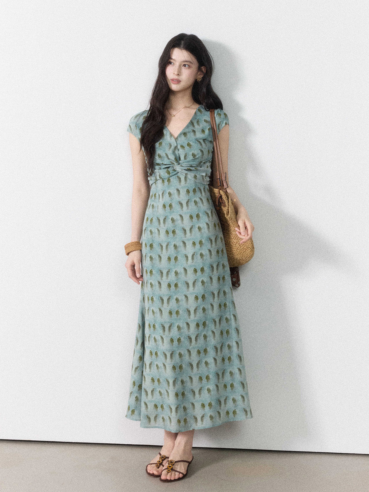 A woman wearing a long, light blue dress with a green leaf pattern and a twisted knot at the waist.