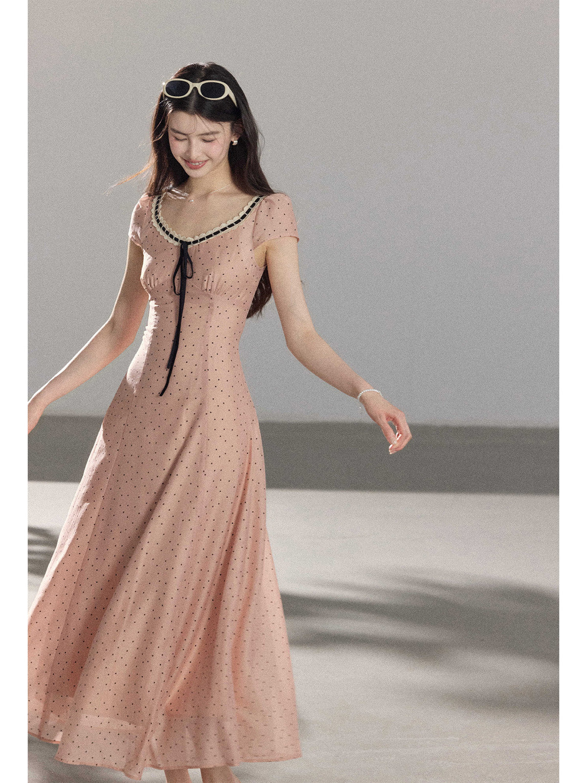 A woman in a pink polka dot dress with lace trim and a black tie at the neckline.