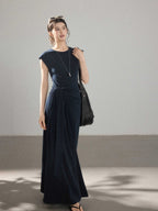 A woman wearing a navy blue long A-line dress with a waist tie and side pleats.