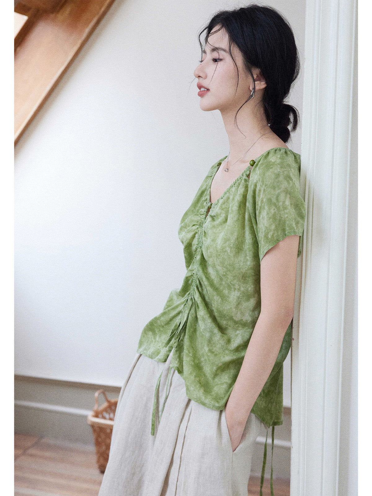 A side view of a woman wearing a green tie-dye top with ruched detailing.