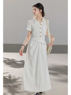 A woman wearing a white A-line dress with a button-front, collar, and twisted waist tie.
