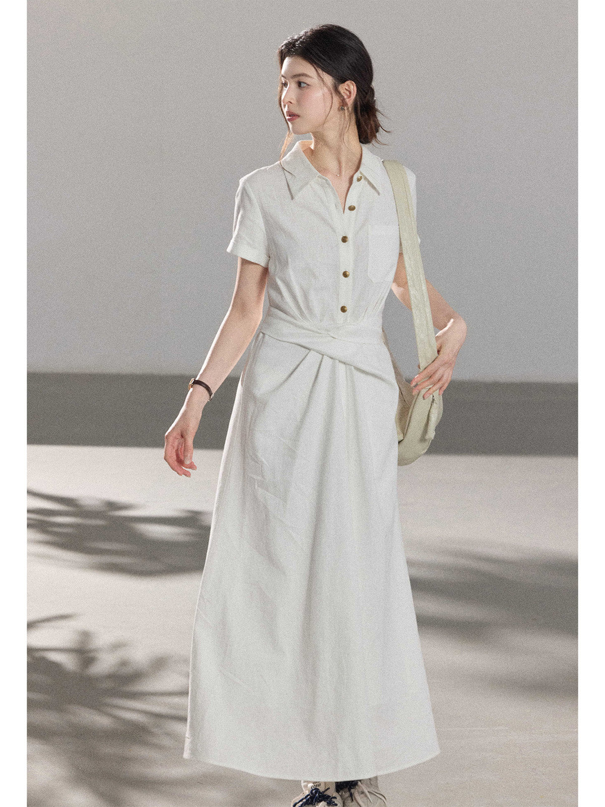 A woman wearing a white A-line dress with a button-front, collar, and twisted waist tie.