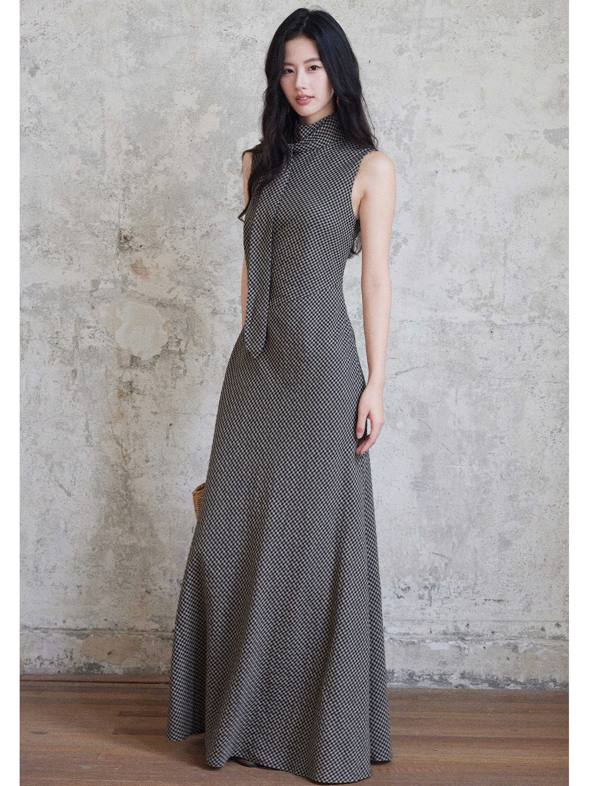 A woman in a sleeveless black gingham floor-length dress with a high neck and tie detail.