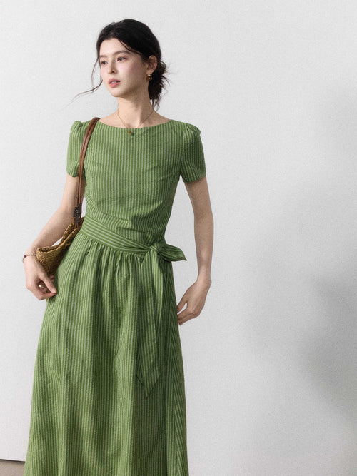 A woman in a long green striped dress with short sleeves, viewed from the side.