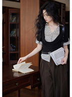 A woman in a black and white striped layered V-neck top with short sleeves, holding a newspaper.
