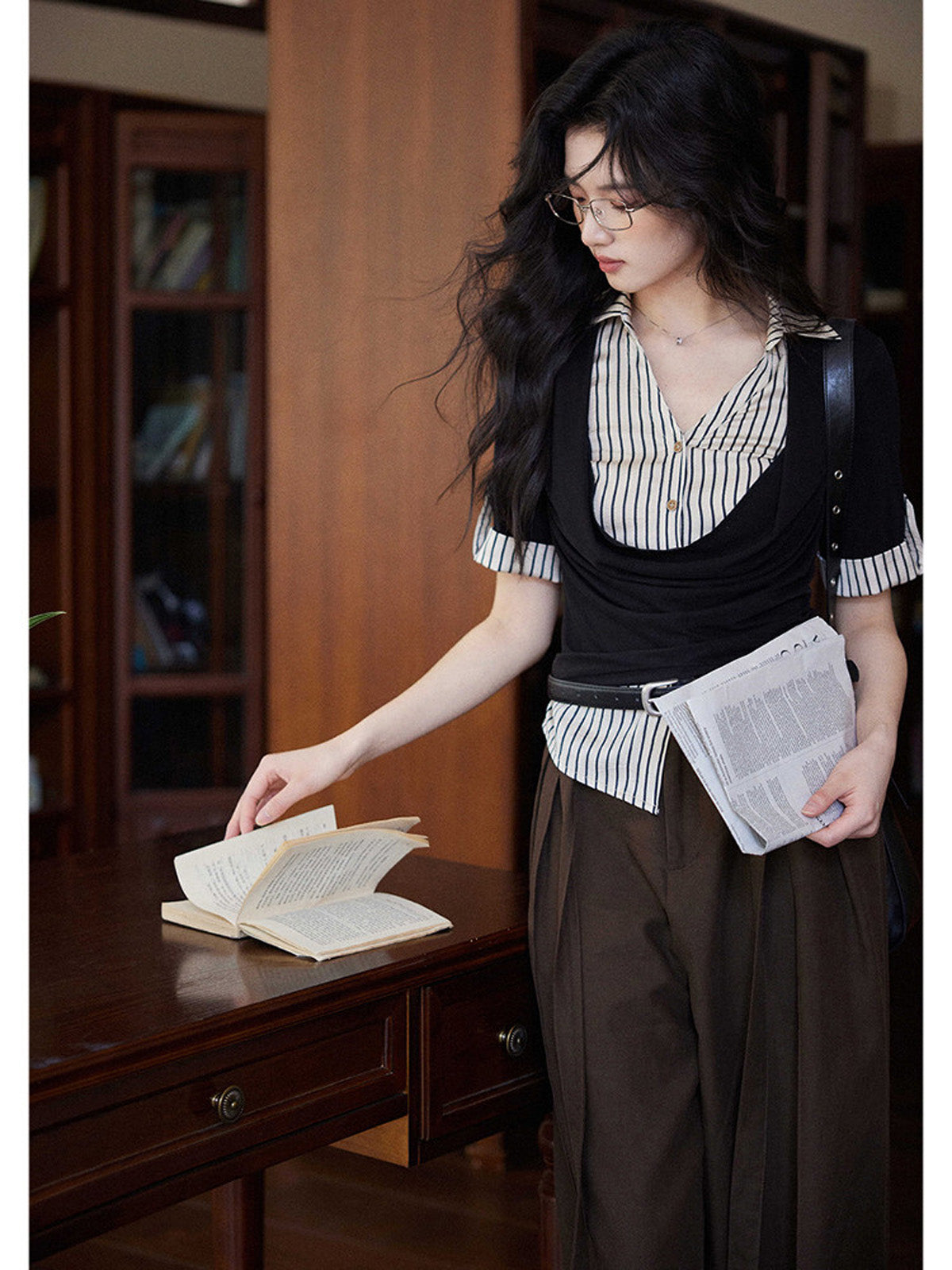 A woman in a black and white striped layered V-neck top with short sleeves, holding a newspaper.