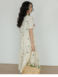 Cream dress featuring embroidered flowers and a gathered waist.
