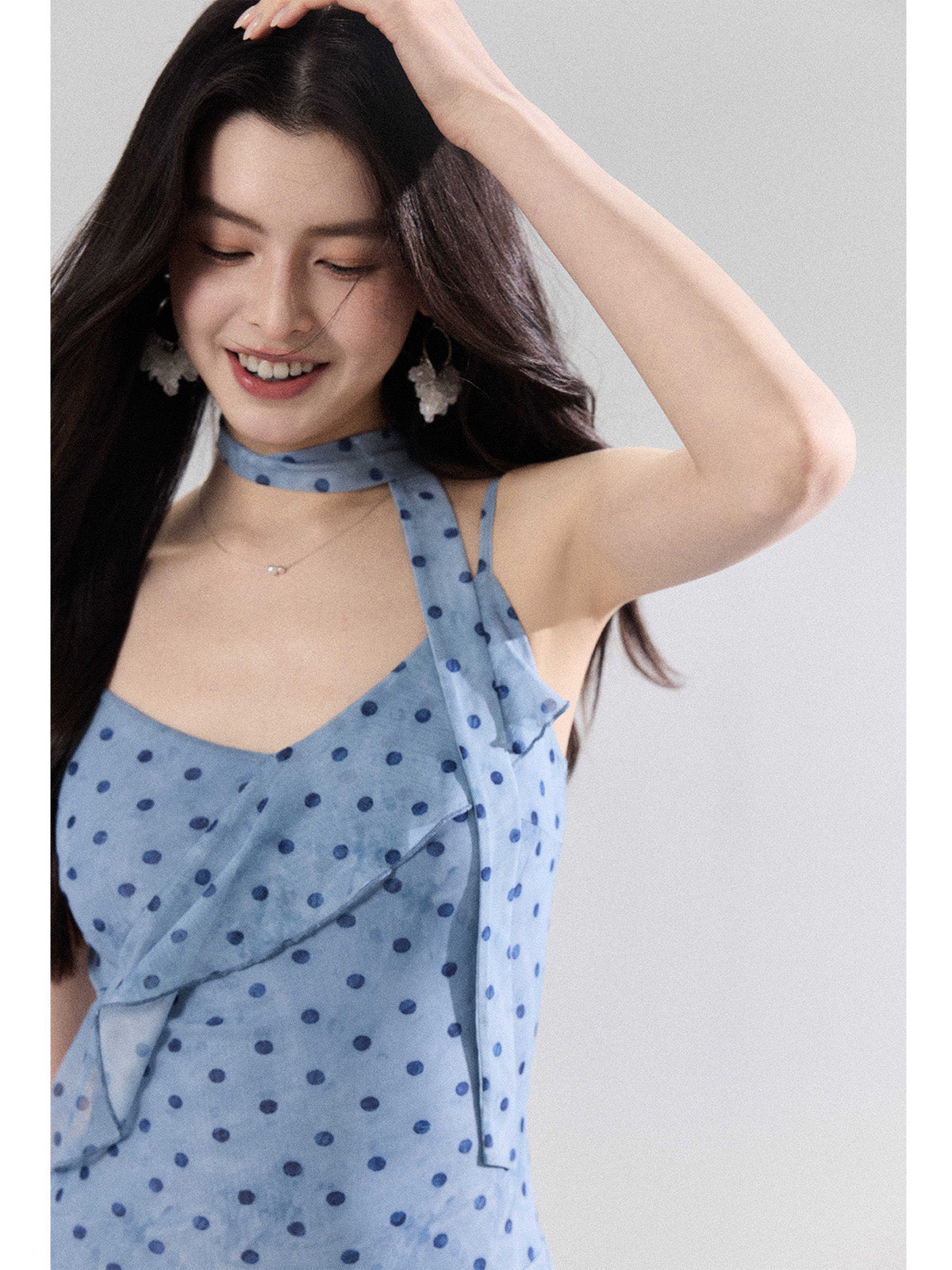 A close-up of a woman wearing a light blue polka dot dress with a ruffled neckline and choker strap.