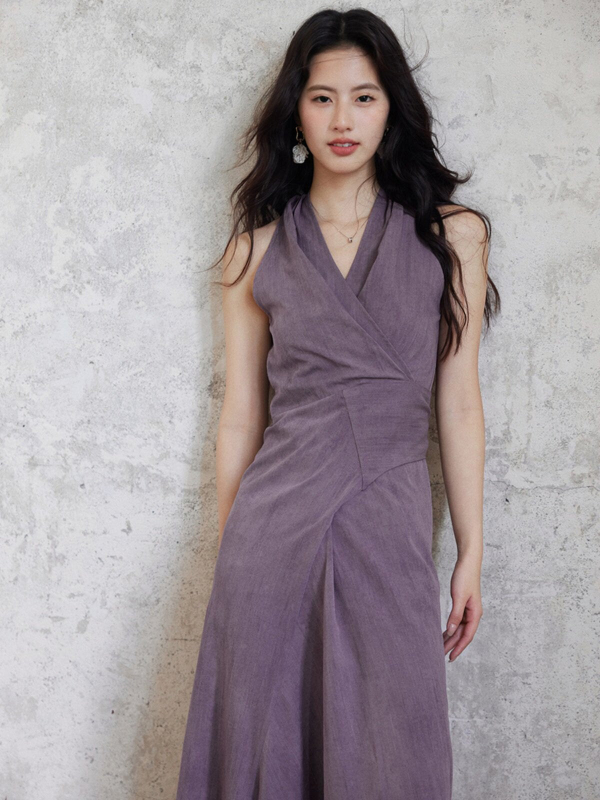 A woman wearing a purple fit-and-flare maxi dress with a V-neck and back tie belt.