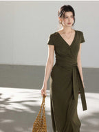A woman in an olive green wrap dress with a V-neck and tie belt, walking.