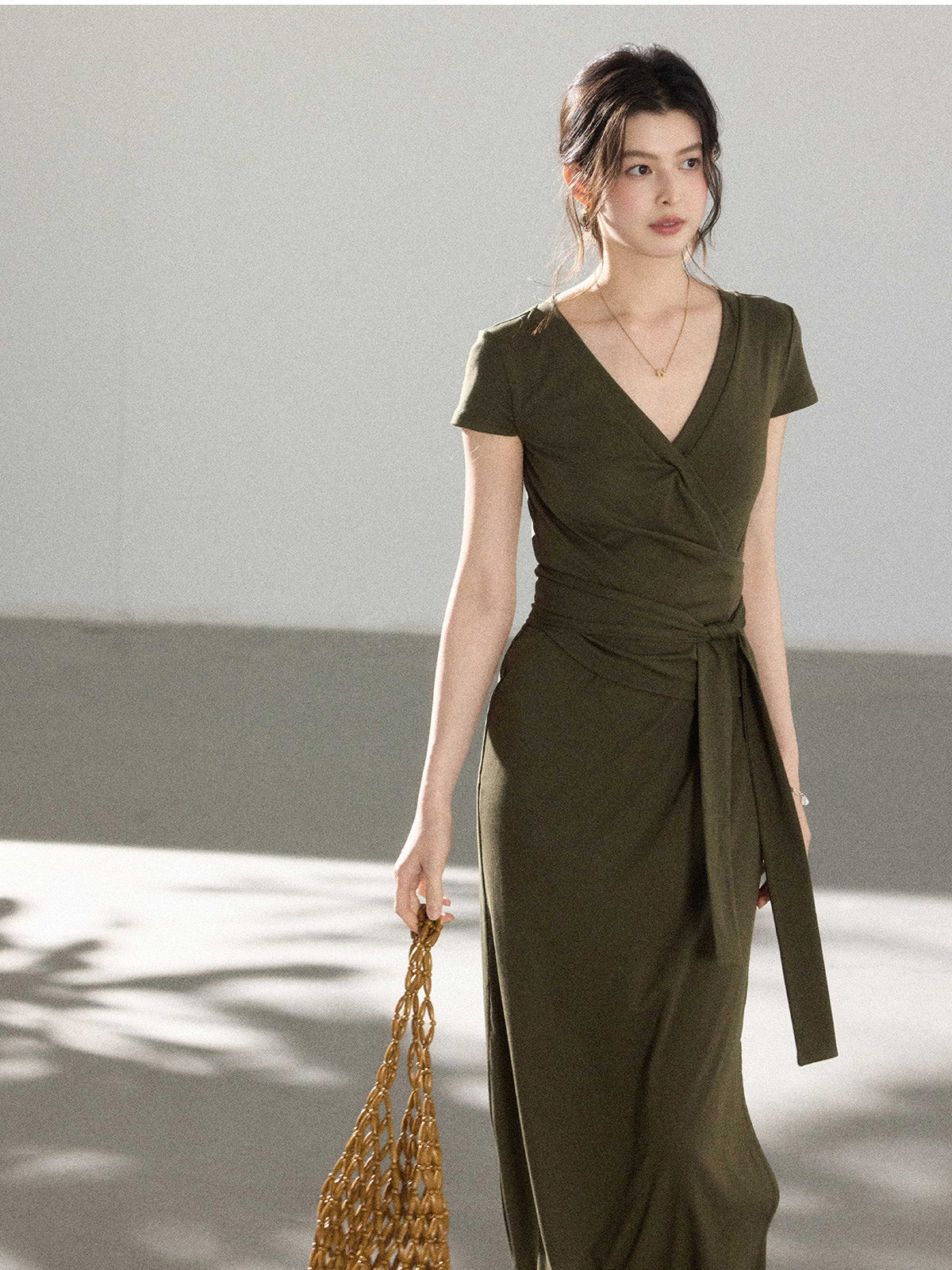 A woman in an olive green wrap dress with a V-neck and tie belt, walking.