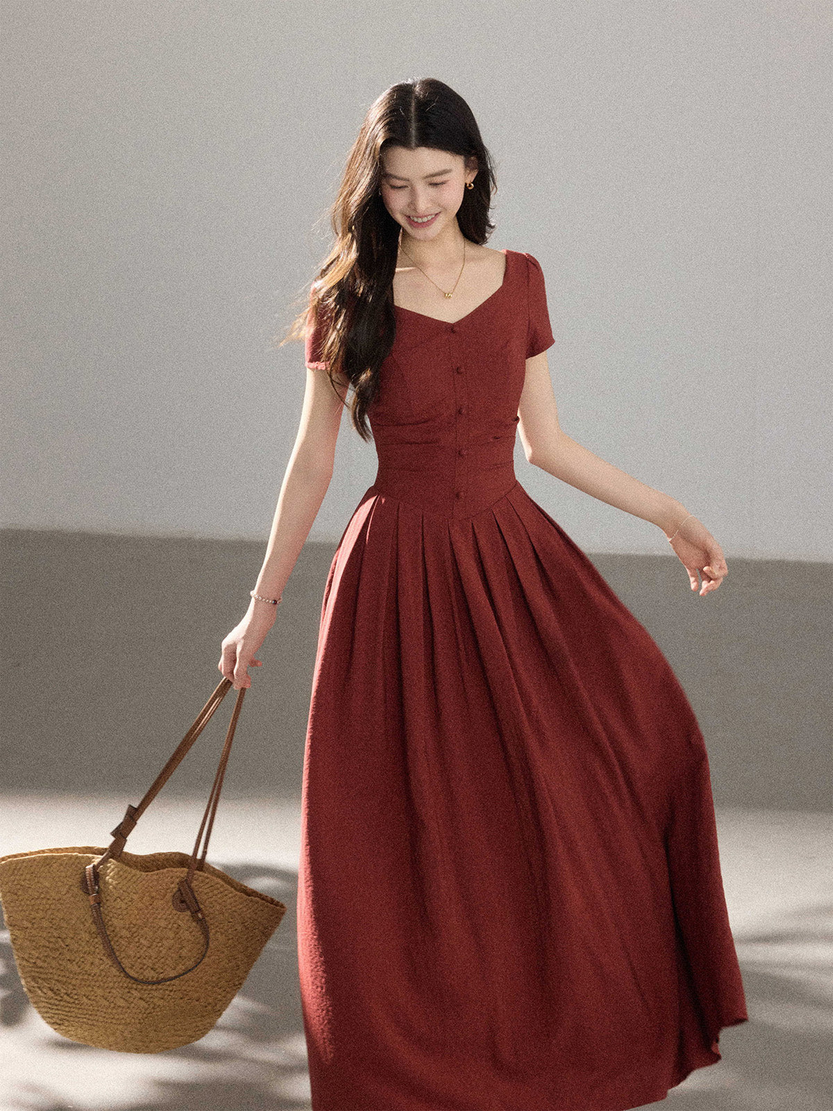 A woman in a red dress with a V-neckline and front buttons, holding a straw bag.