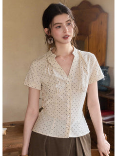 A woman wearing a cream polka dot short-sleeve top with a V-neck and button-front closure.