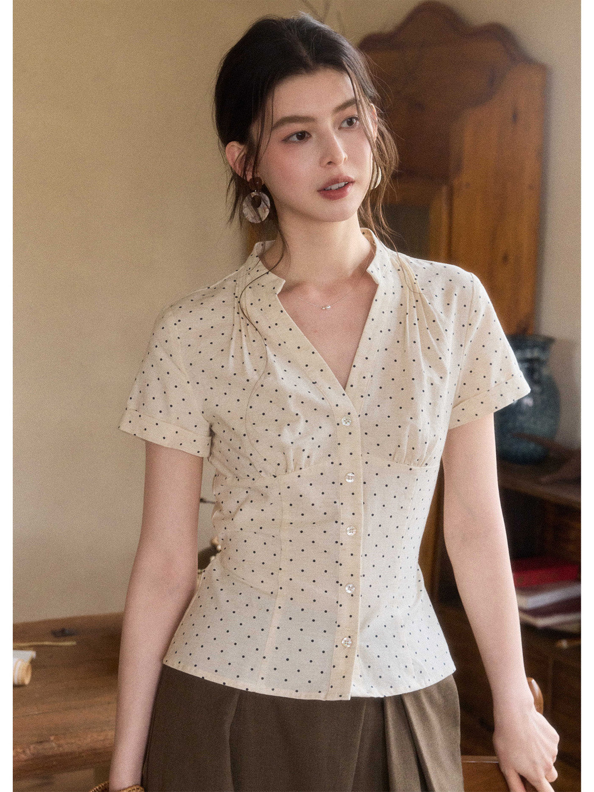 A woman wearing a cream polka dot short-sleeve top with a V-neck and button-front closure.
