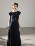 A woman in a navy blue cap-sleeve dress with an asymmetrical hem and side pleats.