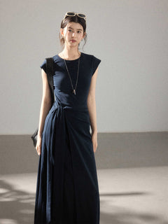 A woman in a navy blue cap-sleeve dress with an asymmetrical hem and side pleats.