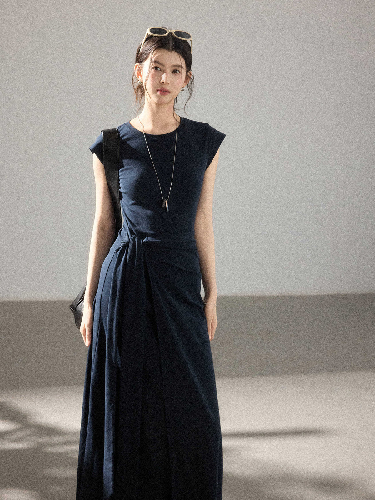 A woman in a navy blue cap-sleeve dress with an asymmetrical hem and side pleats.