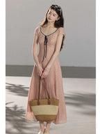A woman in a pink polka dot dress holding a woven tote bag.