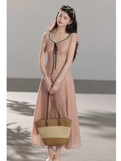 A woman in a pink polka dot dress holding a woven tote bag.