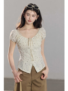 A close-up of a cream polka dot top featuring a square neckline and ruffled details.