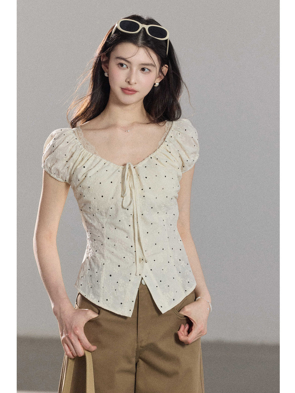 A close-up of a cream polka dot top featuring a square neckline and ruffled details.