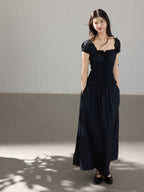 A woman in a black long dress with a square neckline, puff sleeves, and a ruffled waist.